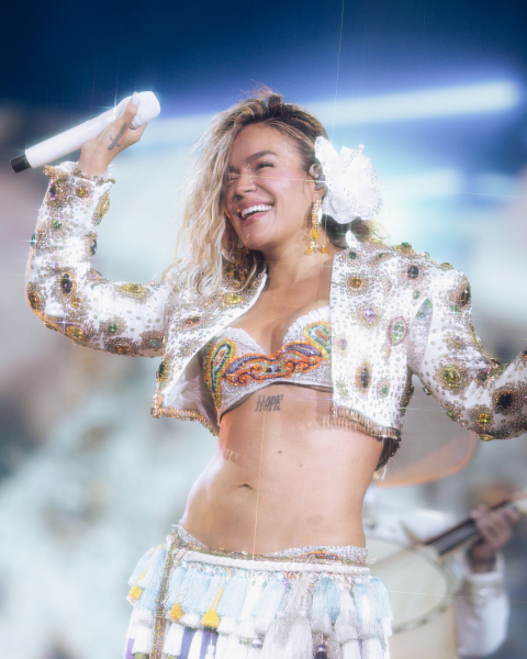 Karol G performs on stage as part of her Viajando Por El Mundo—or Traveling Around the World—tour wearing a white flower...