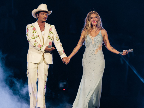 Bruno Mars and Karol G stand on stage holding hands during a performance in Los Angeles for Karol's Viajando Por El...
